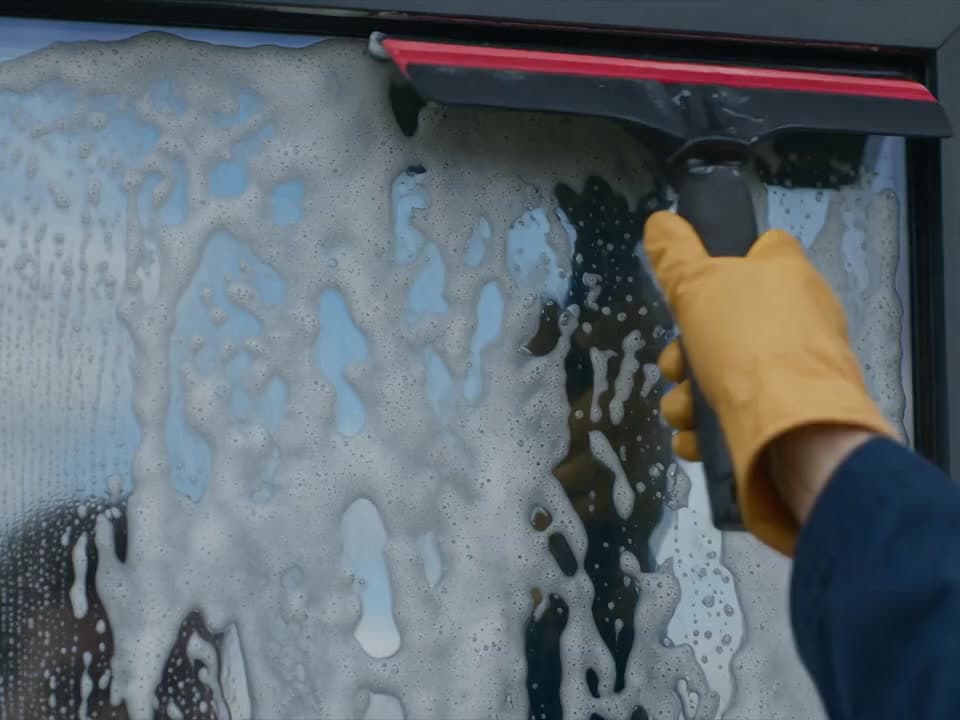 Glazenwasser haalt met een raamtrekker het zeepwater van de beglazing van een bedrijfspand in Zeeland